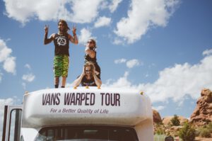 Vans tour van with a dreadlocked band on roof headed to a live nation club.